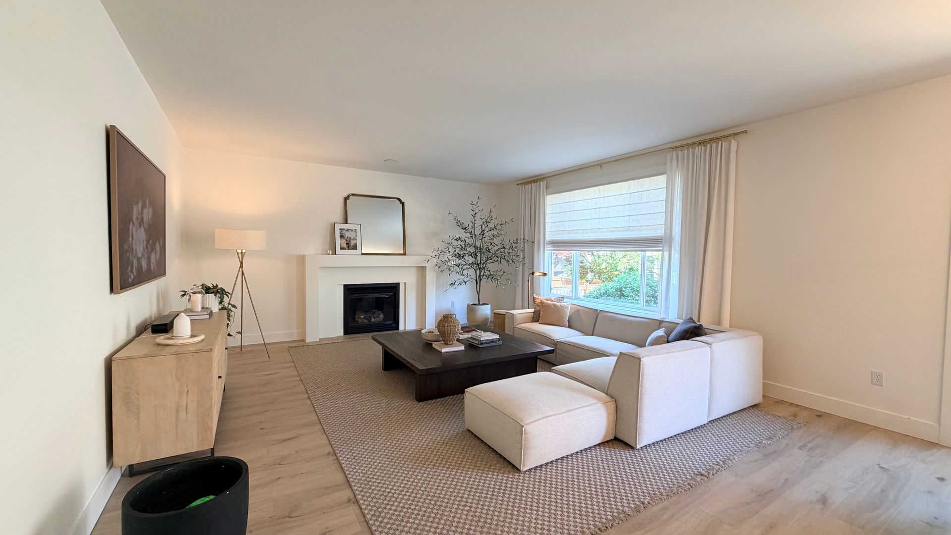 Bright living room with white sectional, fireplace, large window, and neutral decor