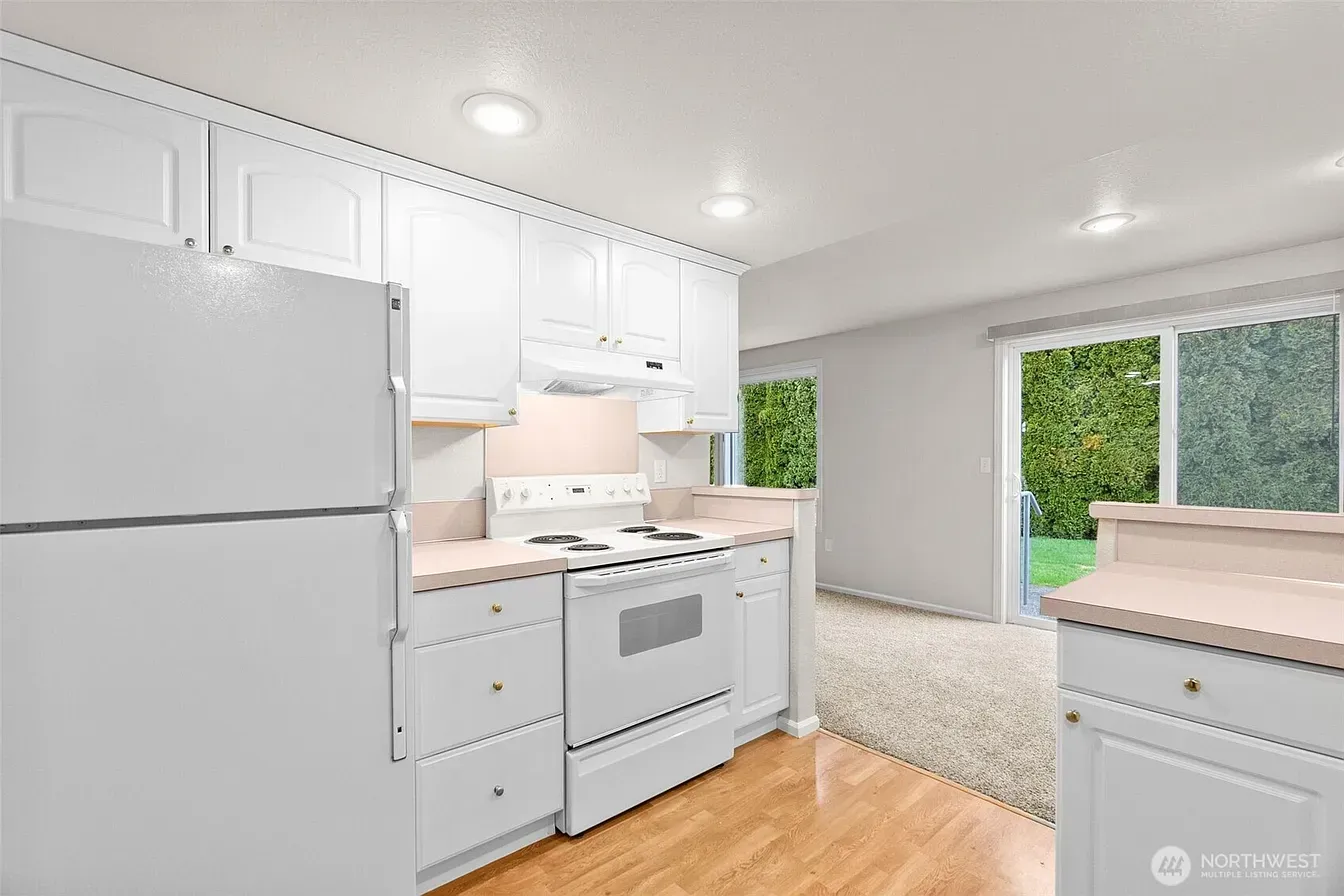 Bright white kitchen with stainless appliances, wood floors, and sliding glass doors to a green yard.