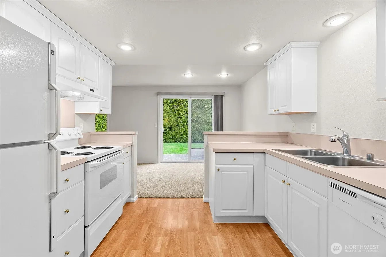 Bright white galley kitchen with wood floors and sliding glass doors to a green yard.