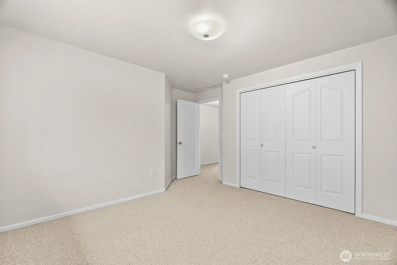 Empty beige bedroom with carpet, white walls, ceiling light, and closet doors