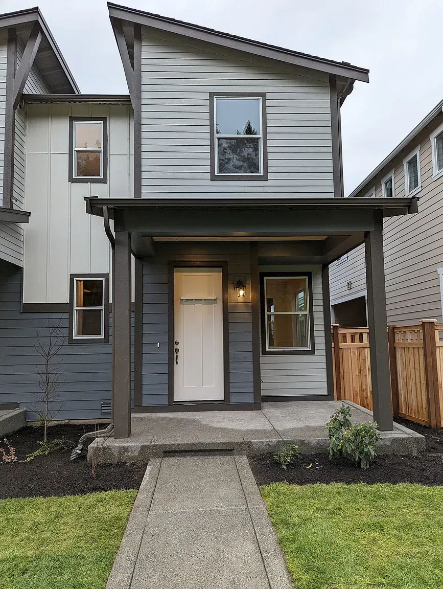 Modern two-story house with gray and white siding, front porch, and small yard with a walkway.