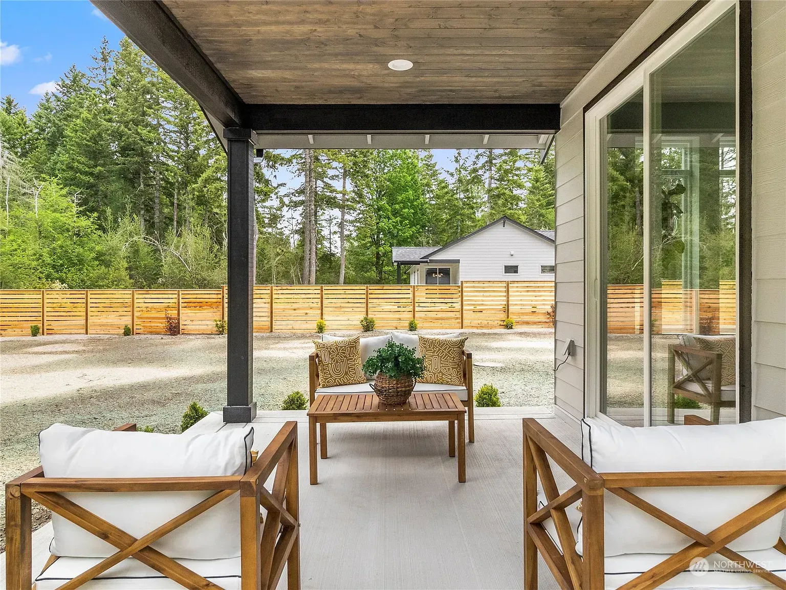 Covered patio with outdoor seating, overlooking a backyard with trees and a house.