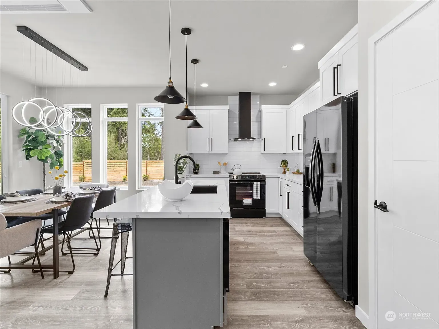 Modern kitchen with white cabinets, gray island, black appliances, and pendant lights.