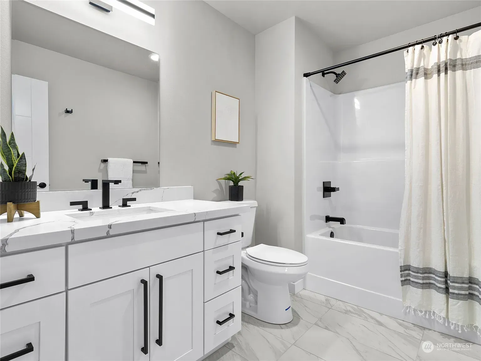White bathroom with marble countertop, black fixtures, and a shower with a patterned curtain.