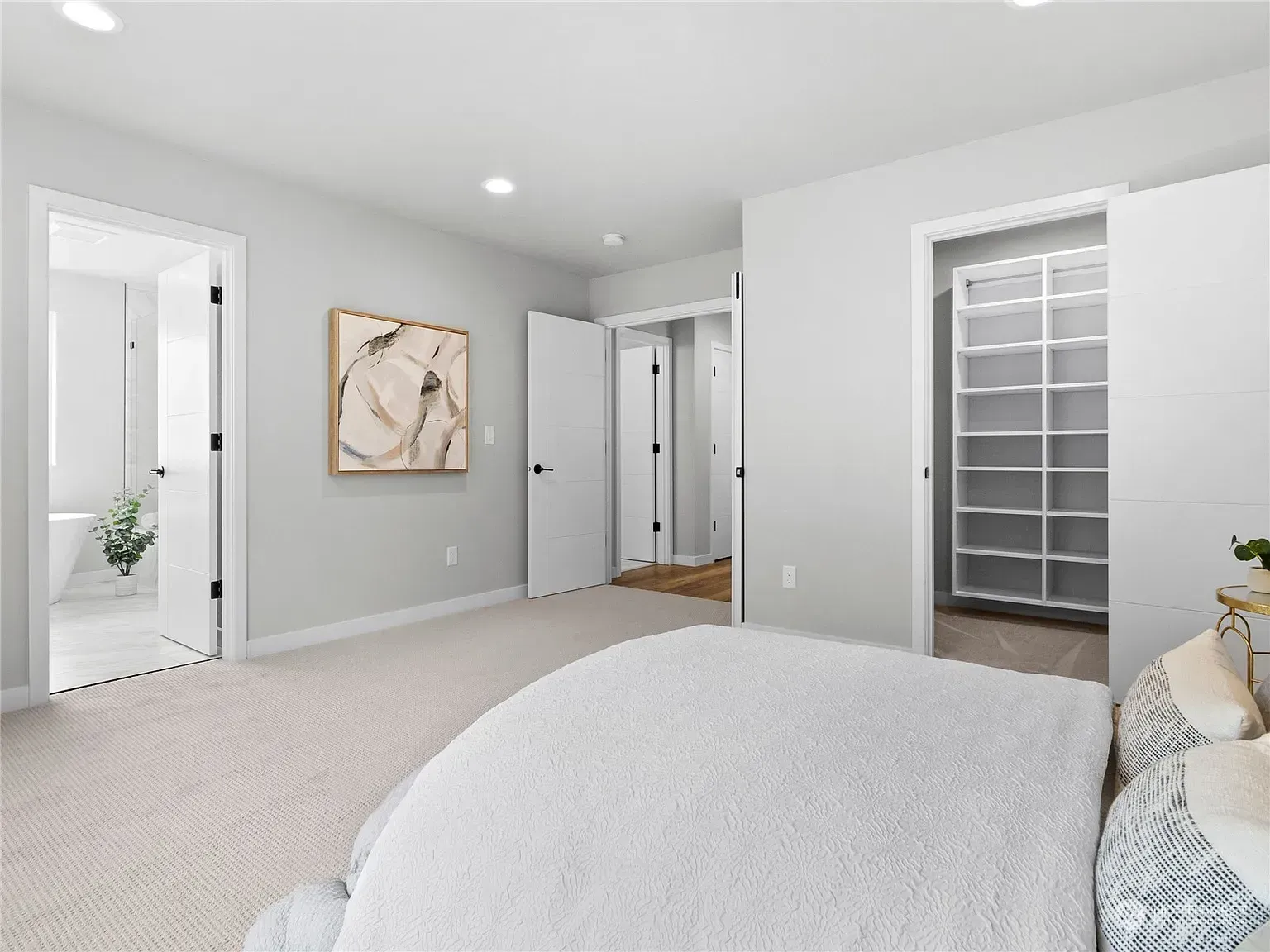 Bedroom with neutral colors, doors leading to bathroom and closet. White carpet and bedding.