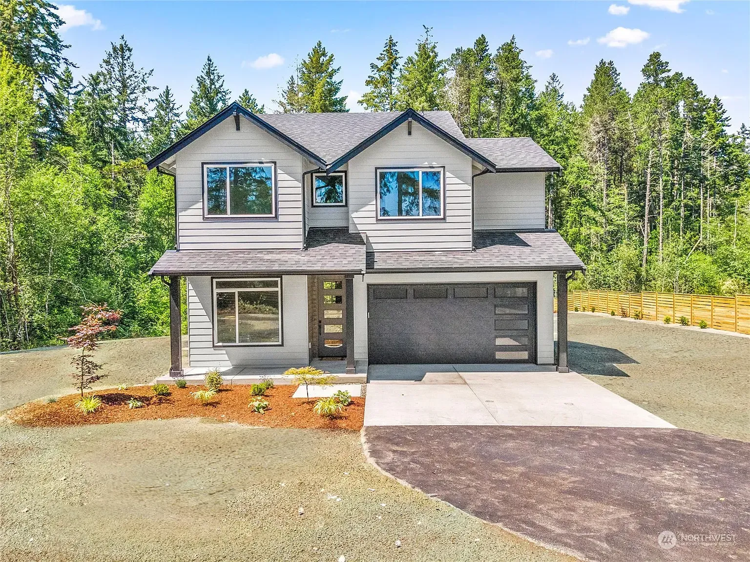 Two-story house with gray siding, black trim, and a black garage door, set in a wooded area.