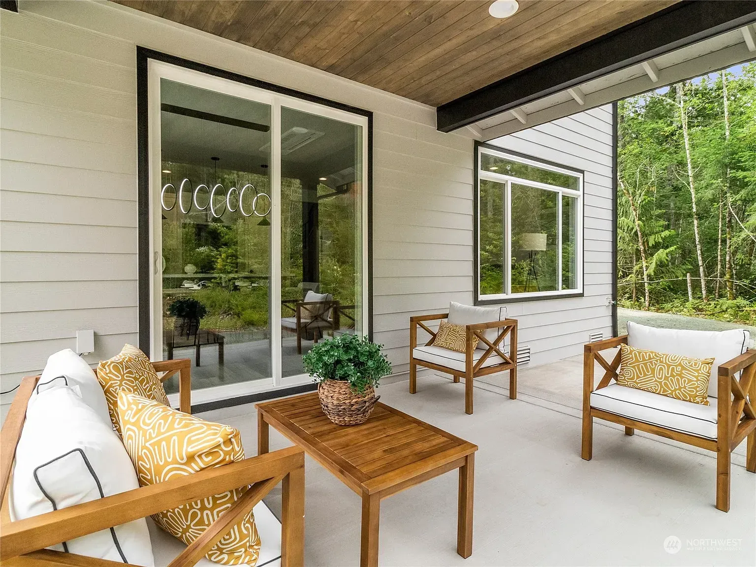 Outdoor patio with wooden furniture, white walls, and a view of trees.