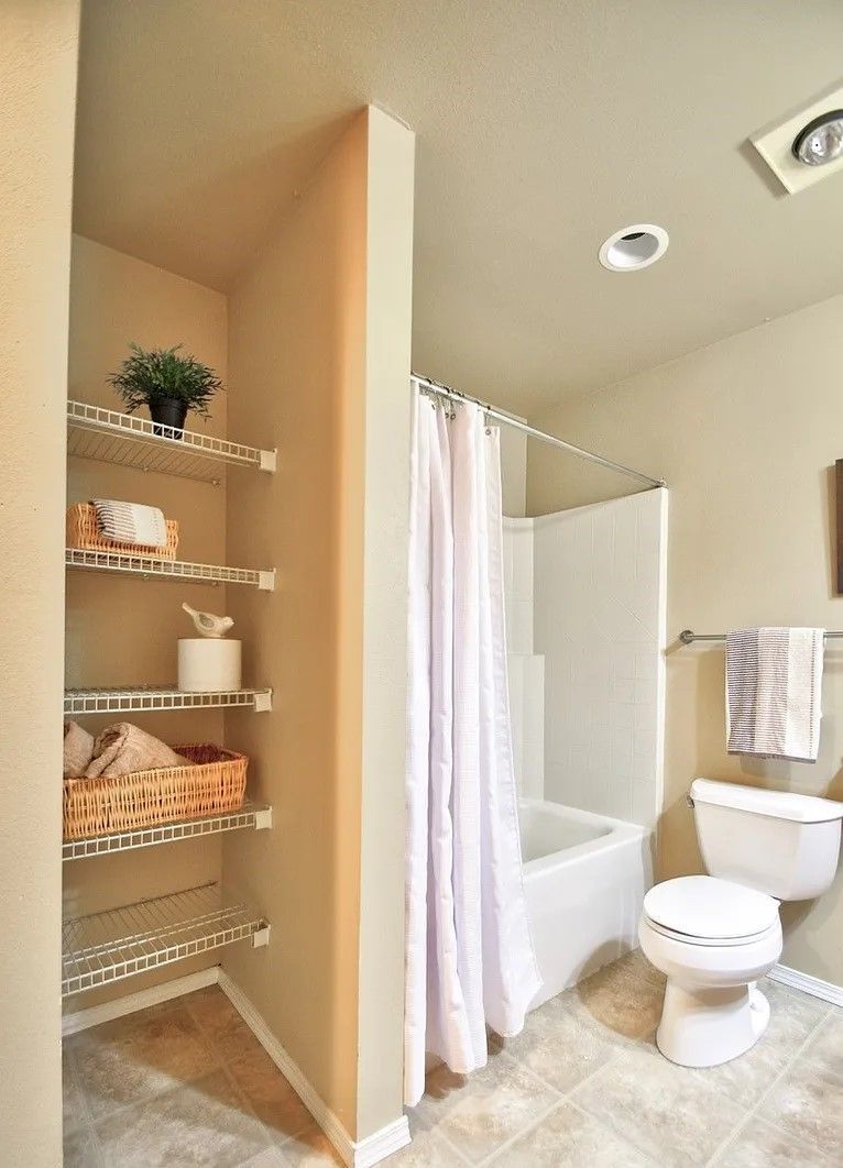 Bathroom with white shower curtain, toilet, and wire shelving with items.
