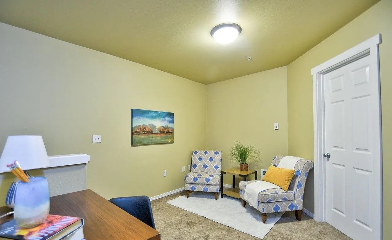Small room with a desk, two patterned armchairs, and a small table with a plant.