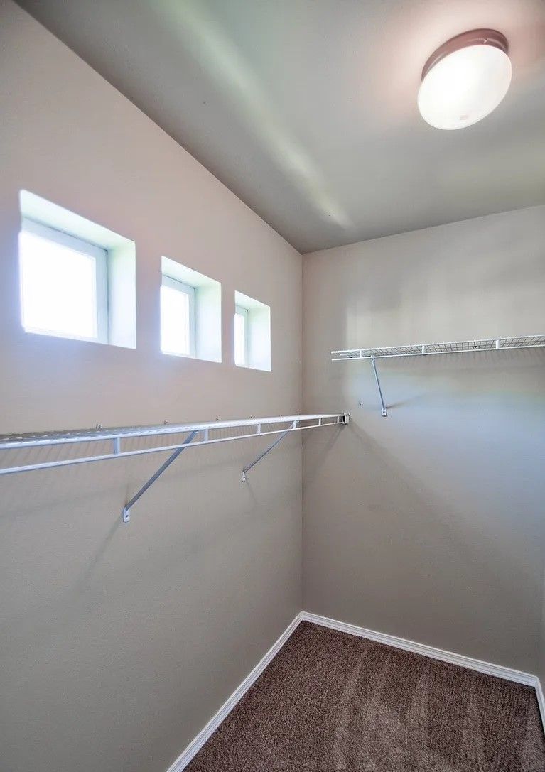Walk-in closet with shelves and carpet. Three small windows allow daylight.