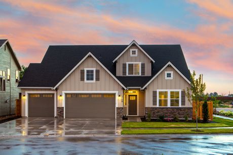 Beige two-story house with dark roof and brown garage doors, in front of a colorful sunset.