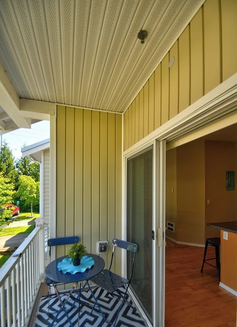 Balcony with table, chairs, and sliding glass door. Yellow walls, patterned rug, and view of trees.